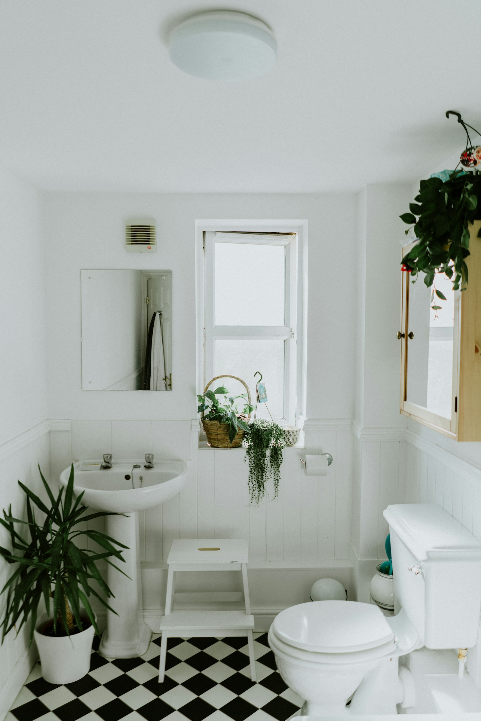 A small white bathroom with beadboard wainscot, a pedestal sink, and a black-and-white tile floor