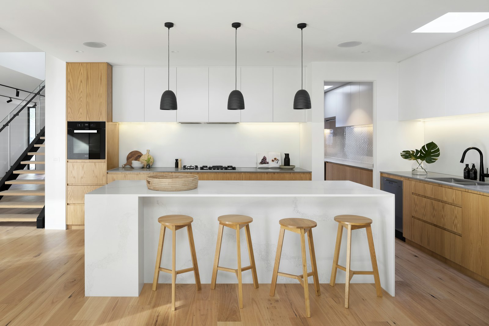 A bright kitchen with white oak floorboards, a stone island, and wood stools
