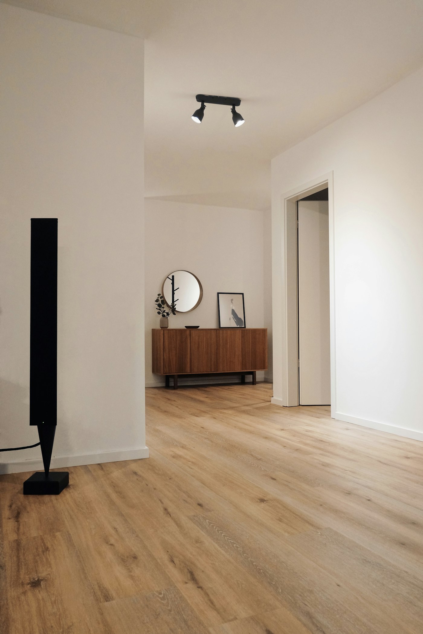 A pale oak floor running through a white hallway toward a walnut sideboard