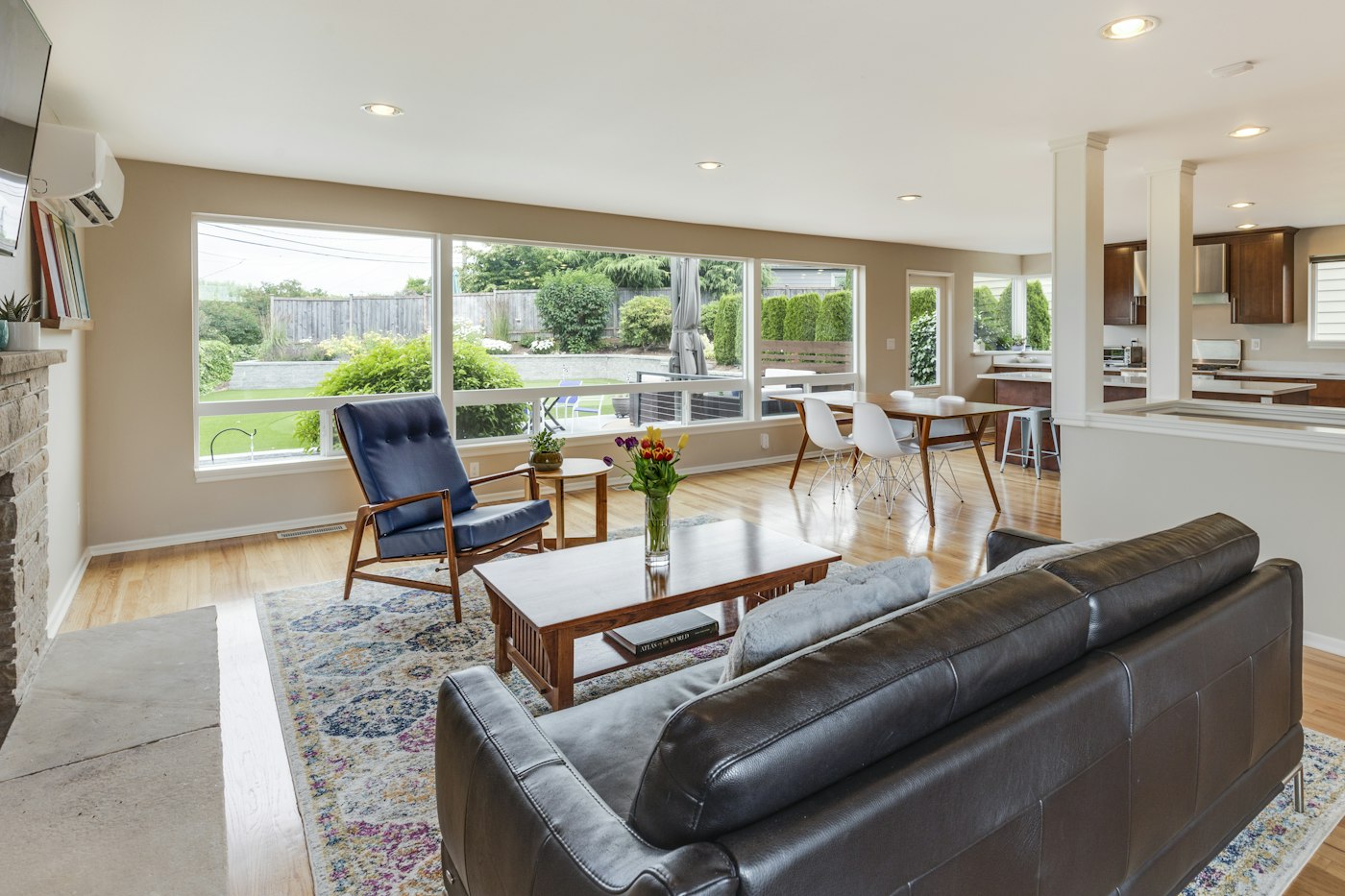 A living room with a leather sofa, a wood dining table, and a kitchen beyond
