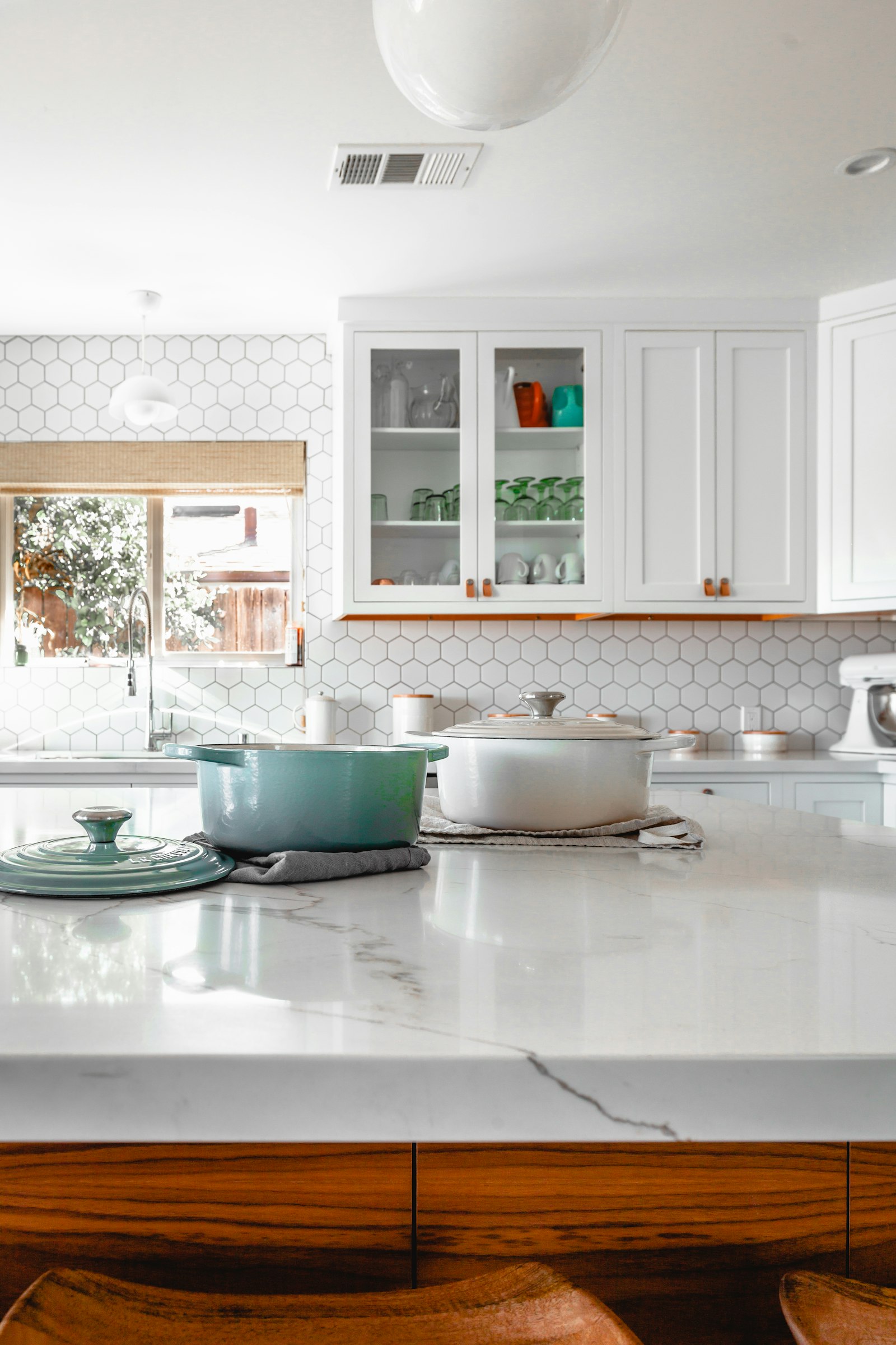 White kitchen cabinets, a marble island, and a walnut base, with pots on the counter