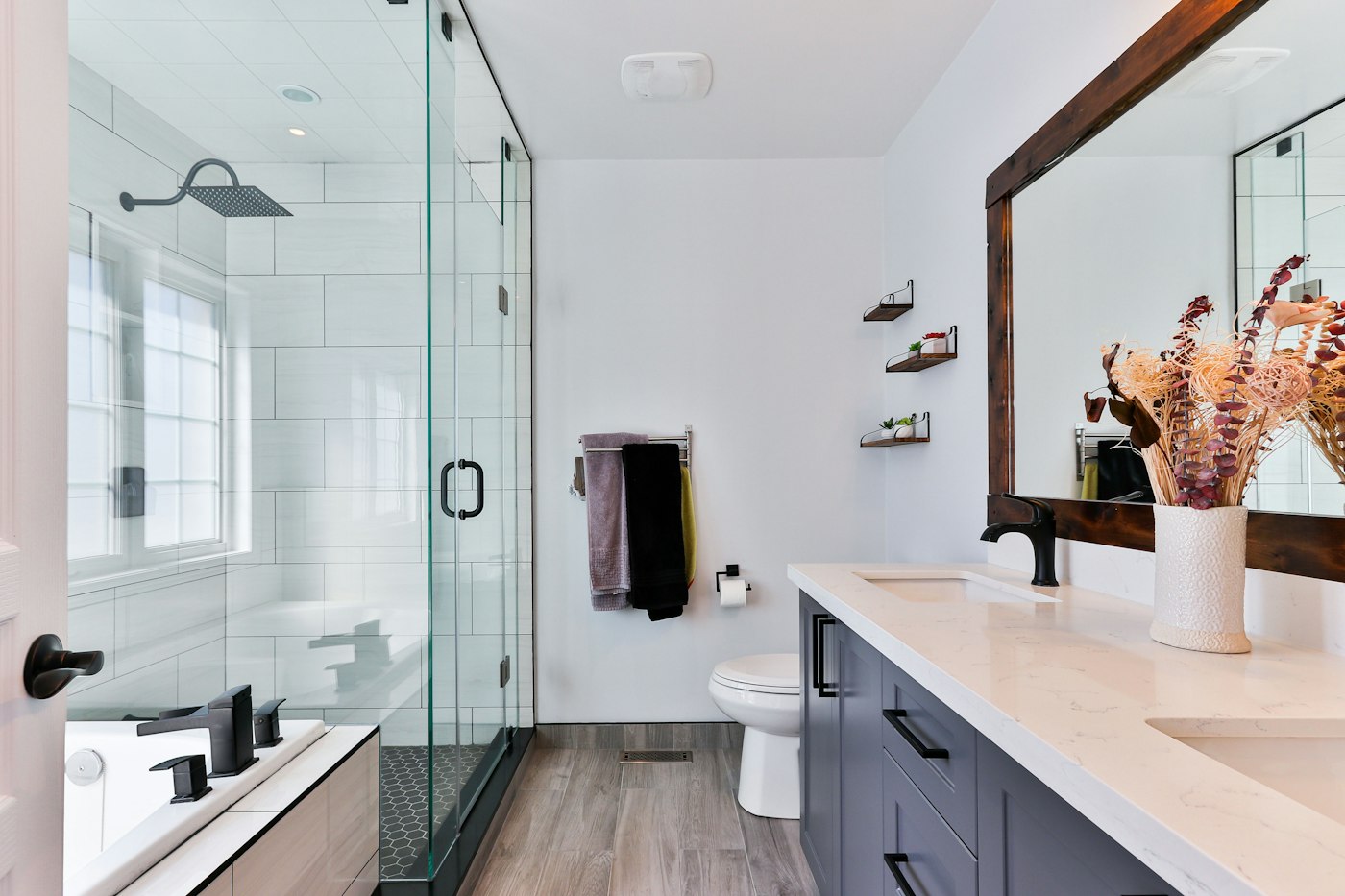 A bathroom vanity in blue-gray cabinets with a white stone top and a glass shower